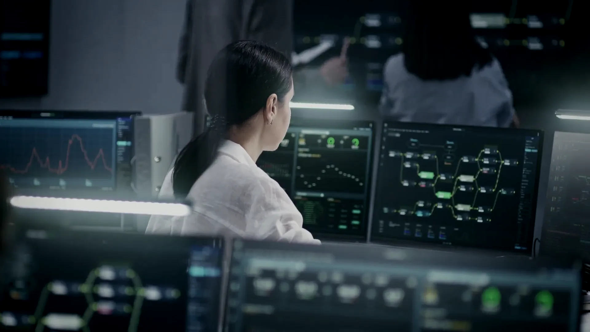 An analyst in profile at a bank of monitors in an operations room.