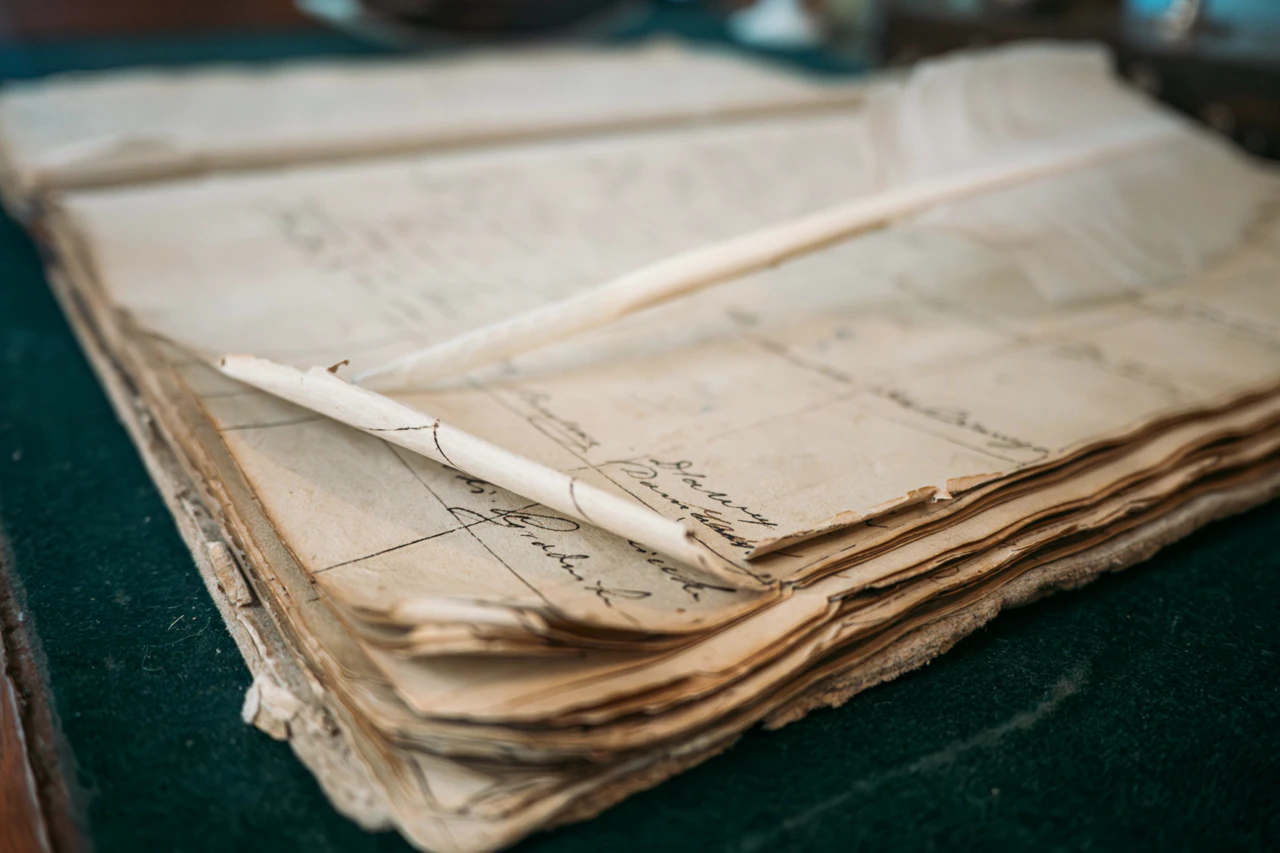 Archive object: a stack of aged handwritten documents with a quill laid across them.