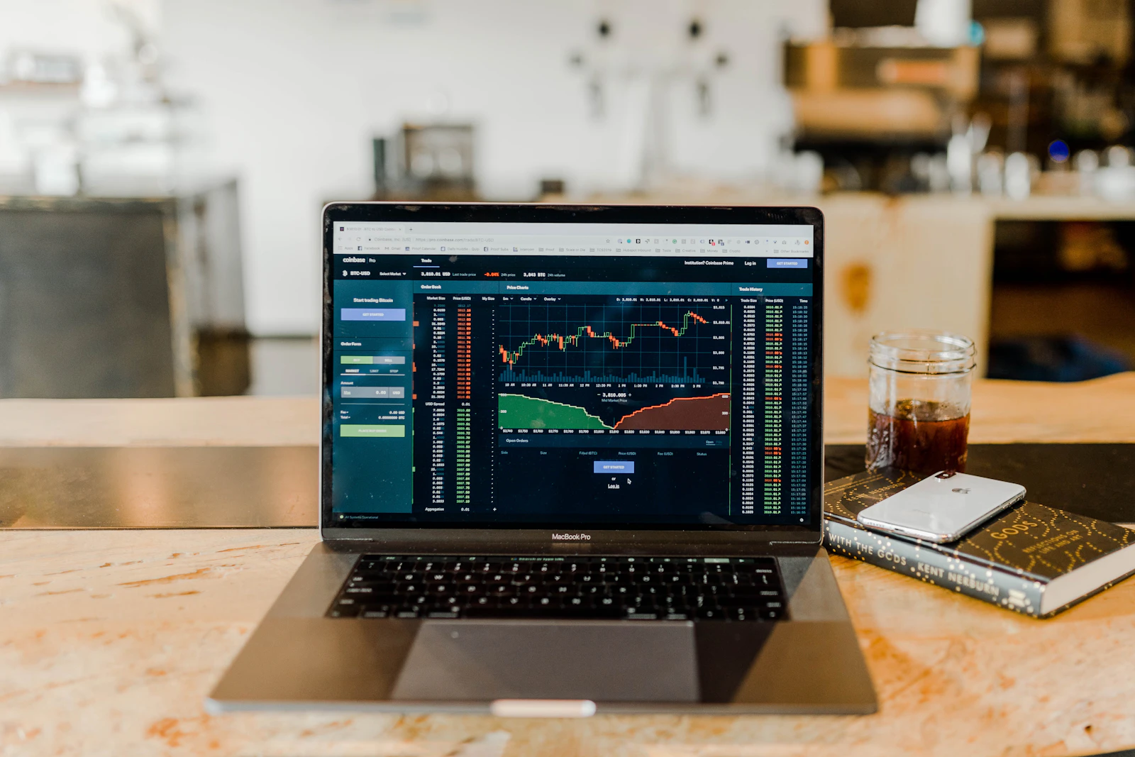 A laptop on a counter showing live trading charts and an order book.