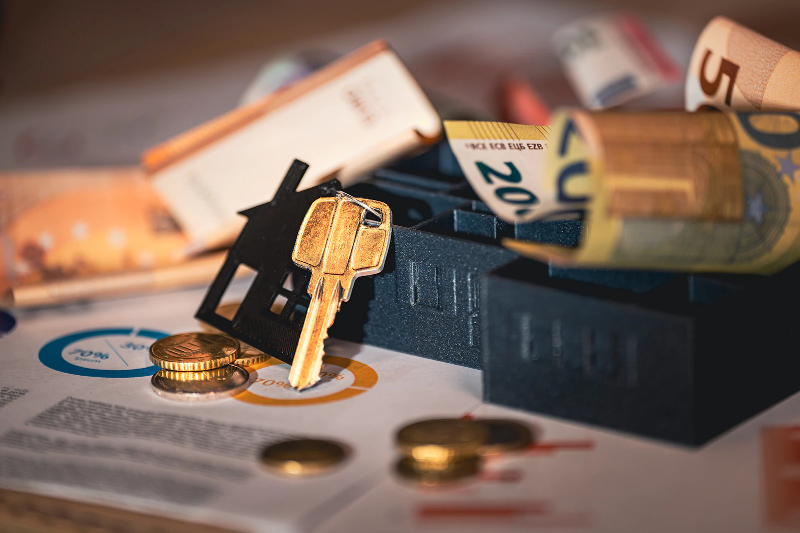 A model house and a house key beside rolled banknotes and printed policy papers.