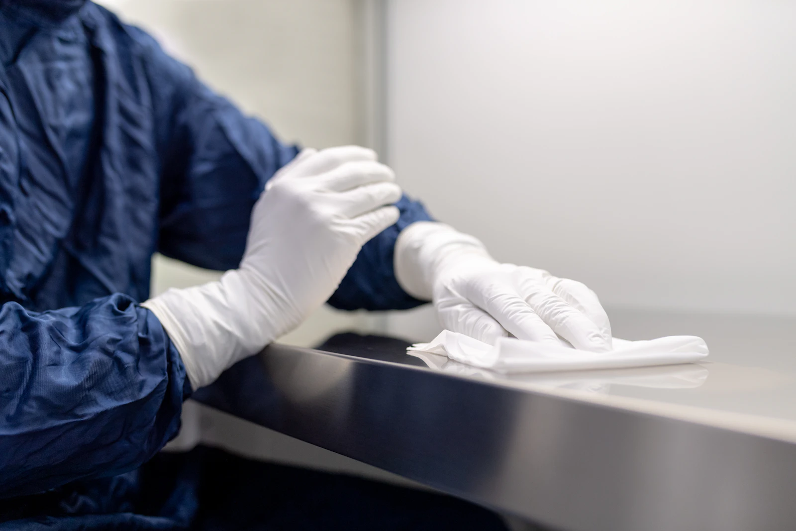Gloved hands wiping a steel bench in a cleanroom.