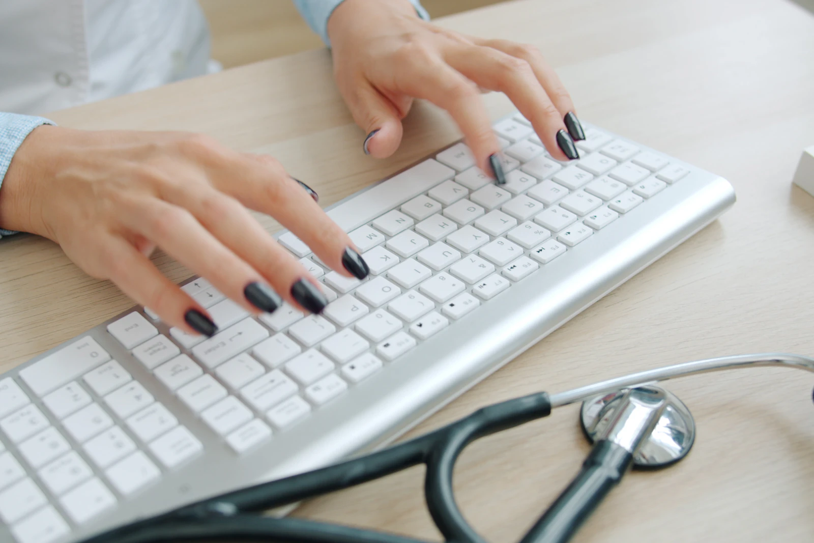 Hands typing on a white keyboard, a stethoscope on the desk beside it.