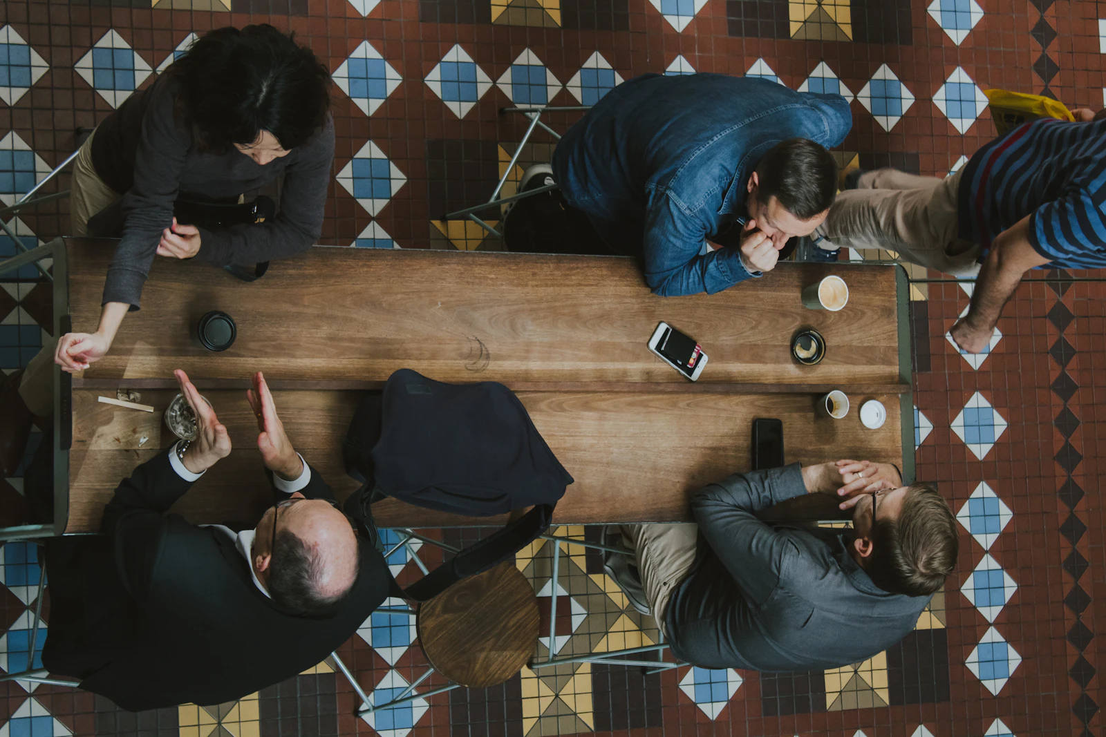 Four people at a wooden table in conversation, seen from directly above, coffee cups between them.