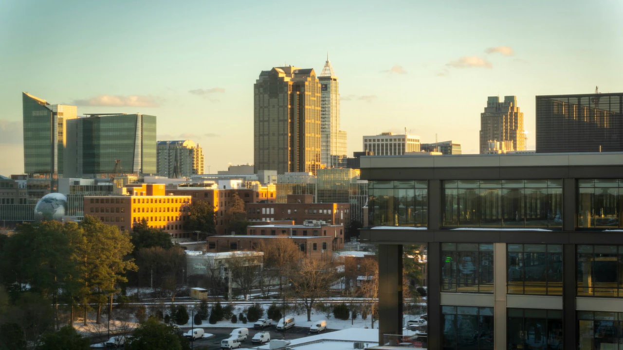 A wide of downtown Raleigh at dusk, the skyline lit against an overcast sky.
