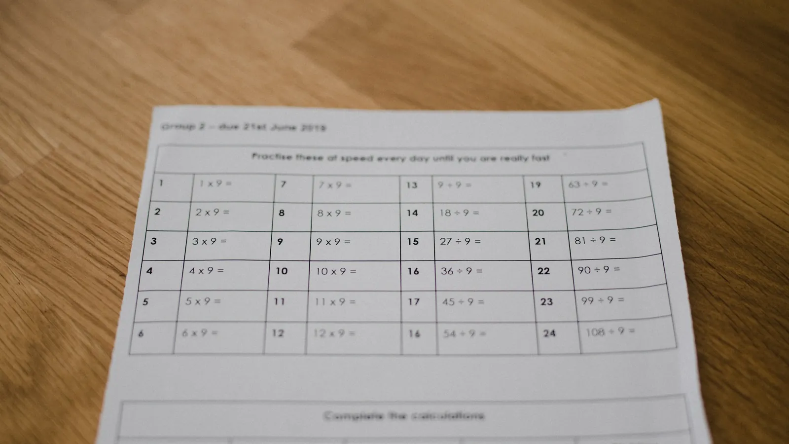 A printed worksheet of numbered rows lying on a wooden desk.