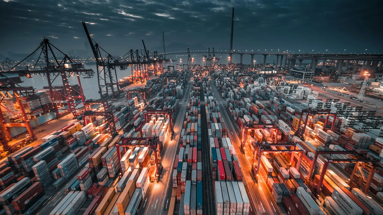 A container port at night from above, stacked containers under working lights.